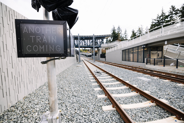 A sign saying "ANOTHER TRAIN COMING" beside train tracks