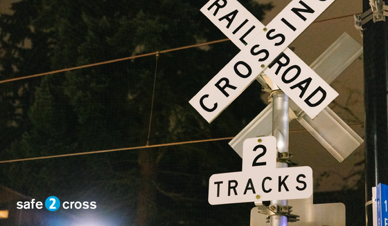 photo of a rail road crossing sign with the phrase "safe to cross" on the bottom left corner