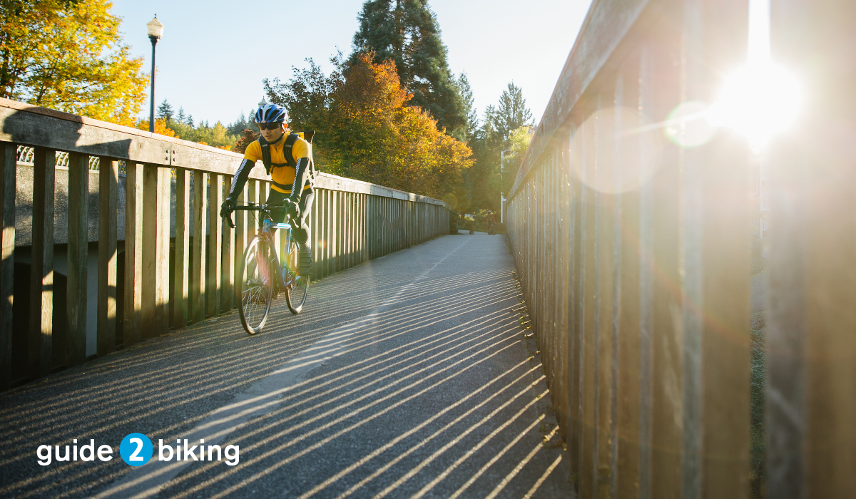 photo of person biking over a bridge into the foreground with the sun in the background