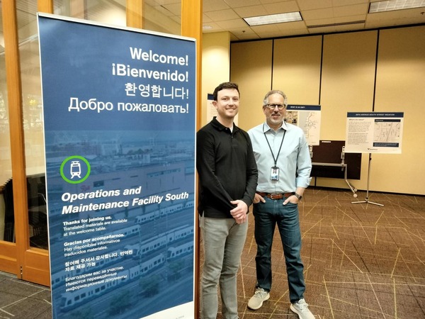 Two men pose next to event welcome banner at a drop-in session. 
