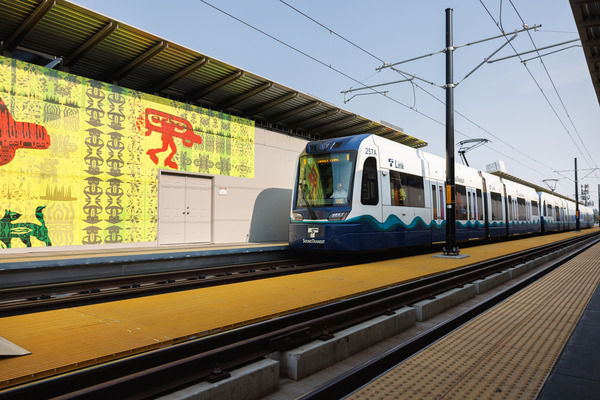 A Link light rail train passing through the NE 130th Infill station. There is temporary art on the walls covering some of the construction. 