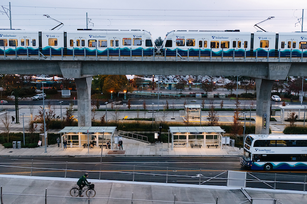 Sound Transit Link light rail enters an elevated station via a guideway with bus shelters underneath. 