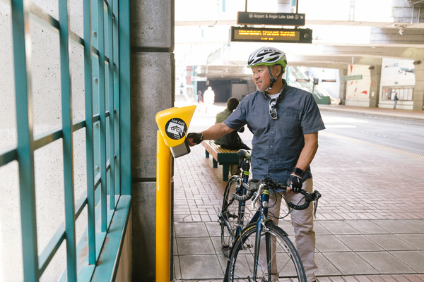 A person holding a bike while tapping their Orca card at a Link light rail station.