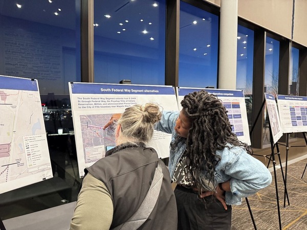 Two people standing in front of an informative board. One person points to a map on the board.