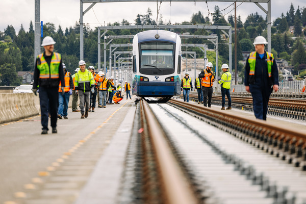 Construction workers observe an unpowered light rail vehicle test as it is towed across Lake Washington 
