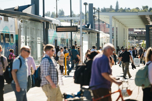 People walking in an outdoor transit center in front of a Sounder train.
