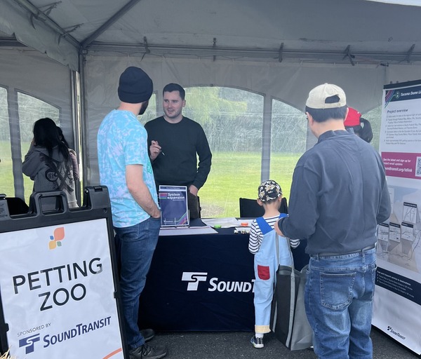 Photo of people talking at a booth that reads "Petting Zoo sponsored by Sound Transit" while others explore the booth.