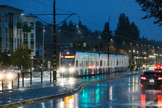 A link light rail train exiting a station in the rain at dusk.