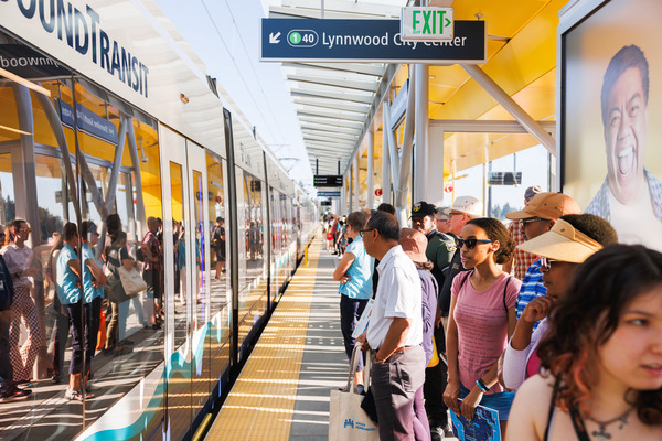 A photo of a crowd of people waiting for a train on a Link light rail platform on a sunny day.
