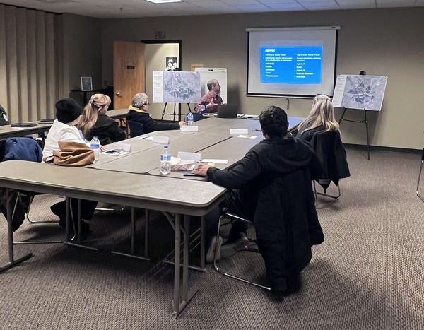 A project staff member discusses future TDLE station planning with five people seated around a table.