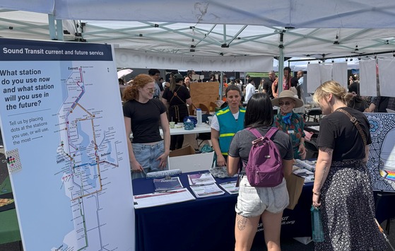 Two event attendees connect with staff and Community Liaisons at Sound Transit informational booth at local summer festival.