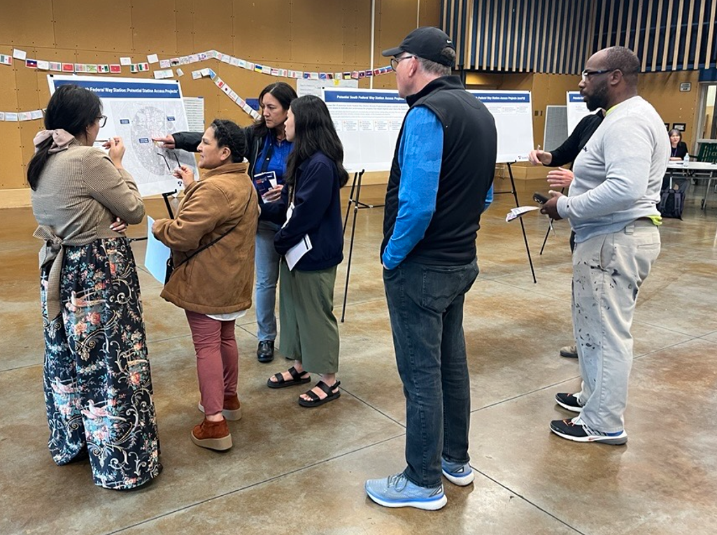 A photo of a group of people discussing a presentation board at a Sound Transit event. 
