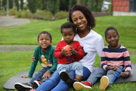 African American mom and children sitting on grass.