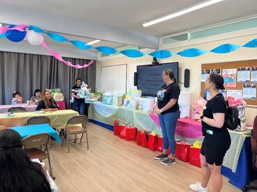 A group of people around tables in a room decorated with streamers and balloons.