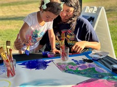 A woman sitting with a young girl painting at a table.