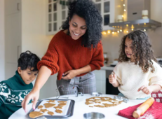 Smiling woman and two children placing cut cookie dough on baking sheets.