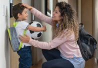 Woman encouraging little boy wearing a backpack and holding a soccer ball.