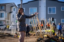 Women talking into a microphone with shovels and people in the background.