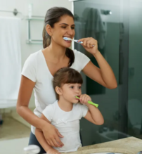 Smiling mom and daughter brushing their teeth in a bathroom.