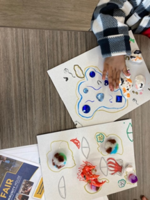 A child's hand touching artwork on a table.