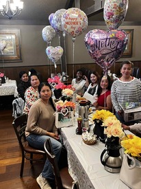 Smiling women posed around a table with "Mother's Day" balloons floating above the table.