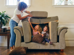 Mom standing at the side of two kids in a couch pillow fort.