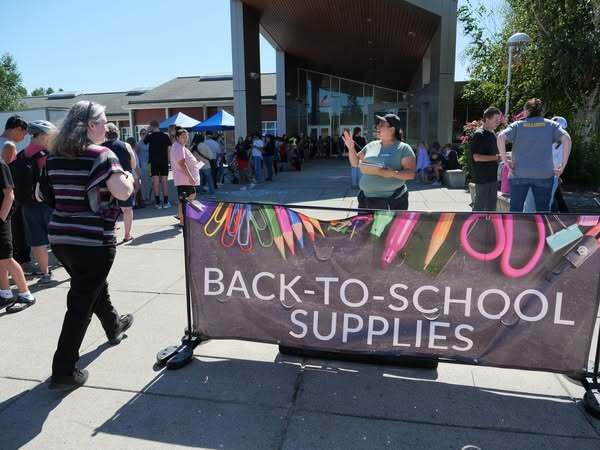 Woman talking to a person who is walking between a line of people and a sign that reads, "Back-to-school supplies."