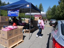 In a school supplies drive-up line, a woman gives a driver a backpack.