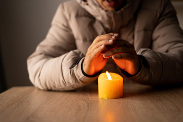 Person seated at a table, warming their hands over a candle.