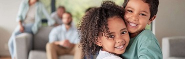 Boy and girl hugging with parents in the background looking on.