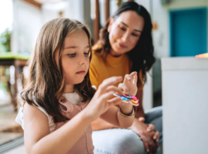 Girl playing with fidget toy and her mom watching.