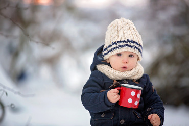 Toddler in winter gear holding a red mug.