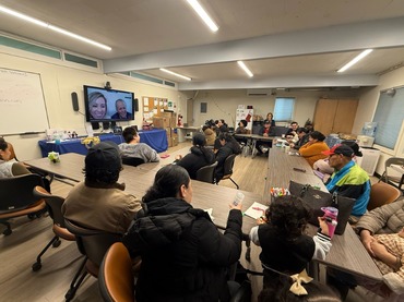 People gathered around tables, watching a presentation on a television.