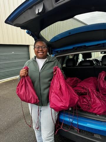 Smiling woman holding care bags in front of a minivan.