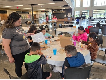 Woman helping children seated around a table with a craft.