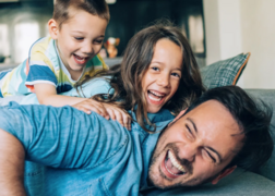 Playful dad laying on his stomach with two laughing kids on his back.