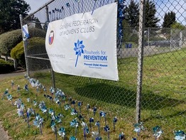 Pinwheel in the lawn in front of a sign hanging from a chain link fence.