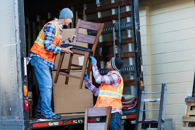 Two movers in safety vests load a chair into a moving truck.