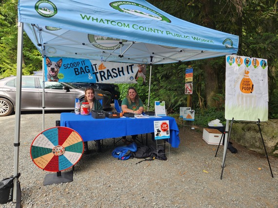 Staff sitting at outreach booth at a Lake Whatcom Park Pet Waste Pop Up event