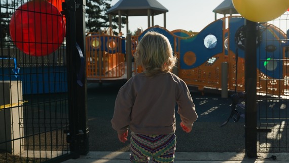 Small child walking through the entry gates of a playground.
