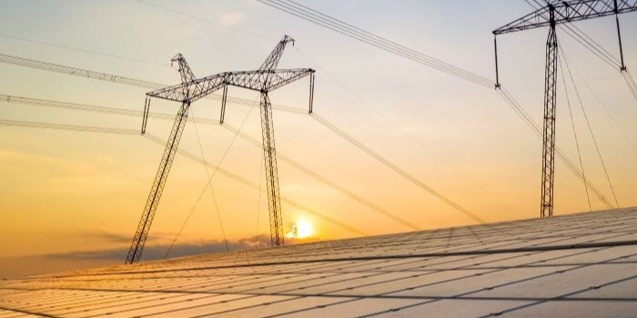 Solar panels producing electricity, with high transmission lines overhead. 