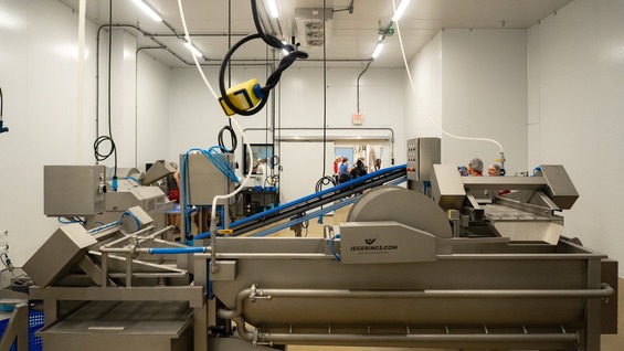 Food machinery at the Foodshed facility and people in hairnets in the background