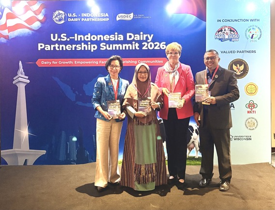IABC International Consultant stands with other representatives in front of a display with representatives and they smile while holding up papers.