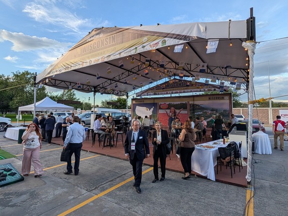 People in formal wear talk in groups at tables underneath a large outdoor tent in a parking lot.