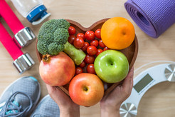 Picture of fruits and vegetables in a heart-shaped bowl with exercise equipment nearby. 