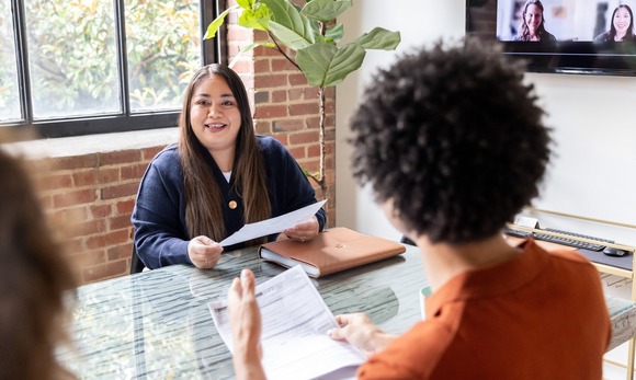 Woman holds document in a hybrid meeting with co-workers in the office.