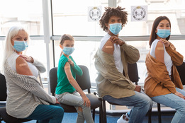 Four people showing arms with band aids to indicate vaccine