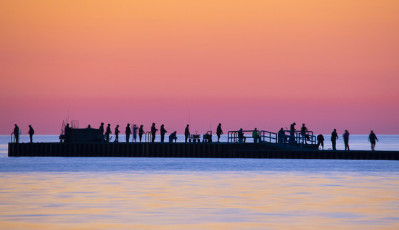 A group of people out on a pier in Lake Michigan, fishing at sunrise.