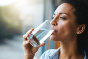A woman holds a glass of water up to her mouth as if she's about to take a drink.