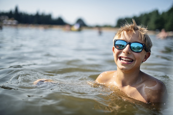 A kid smiles as he swims in a lake.